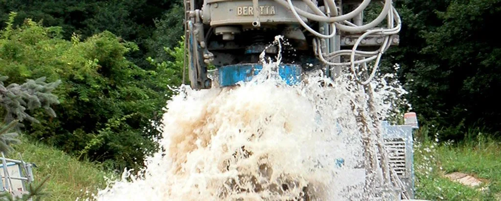 Wasser schießt schäumend aus dem Bohrloch unter einer Bohranlage